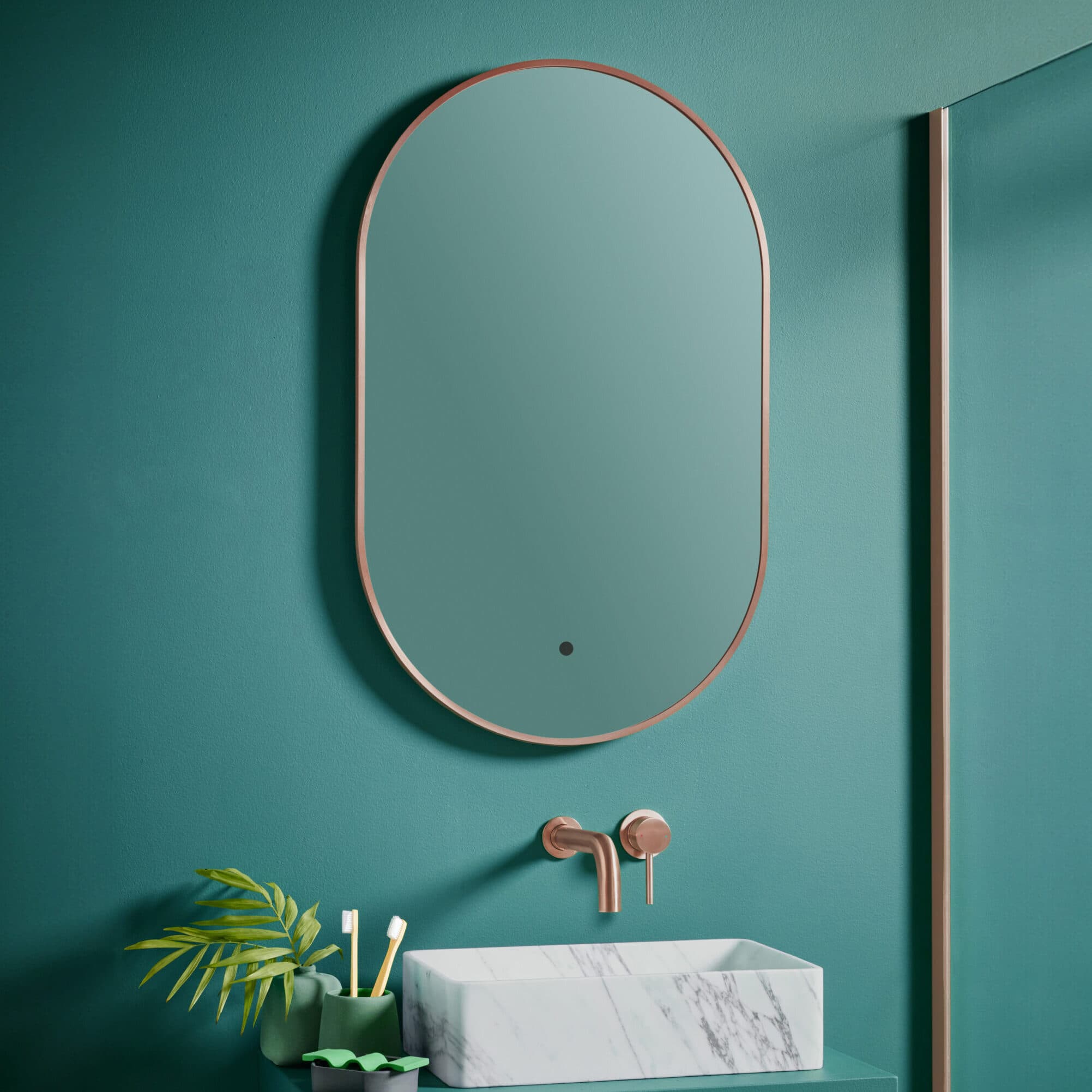 Bronze-coloured oval mirror and wall tap against a deep green wall above a veined basin.