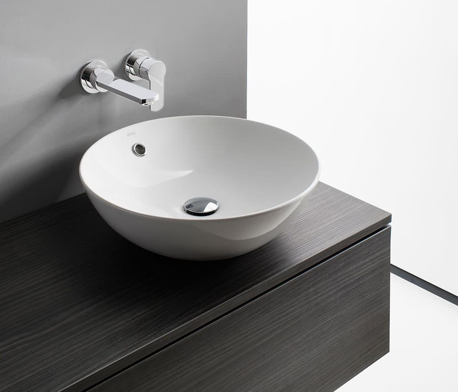 Round white countertop basin on a dark woodgrain top with wall-mounted chrome taps